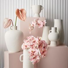 several white vases with pink flowers in them on a shelf next to each other