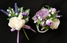 two boutonnieres with purple and white flowers are on a black tablecloth