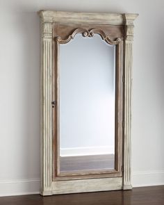 an antique white mirror is on the floor next to a wooden cabinet and hardwood floors