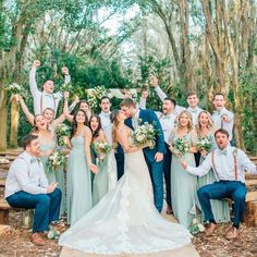 a large group of people standing around each other in front of some trees and bushes