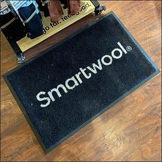 a black door mat that says smartwool on the floor next to a suitcase