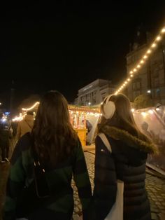 two girls walking down the street at night with headphones on their ears and lights in the background