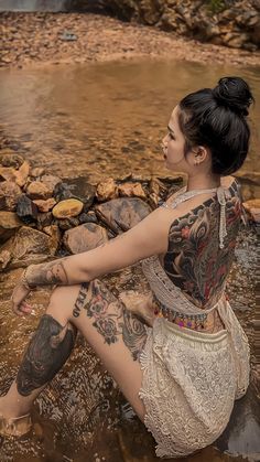 a woman sitting in the water with tattoos on her arm and leg, next to some rocks