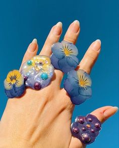 a woman's hand is holding three rings with flowers on them and beads in the middle