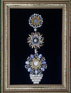 an ornate frame with three different jewels on the front and back of it, hanging from a wall