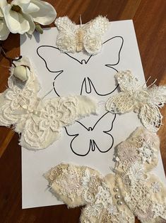 several pieces of lace are laid out on a piece of paper with flowers in the background