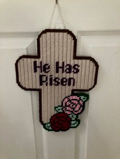 a cross hanging on the front door with flowers and words written in black ink that says he has risen