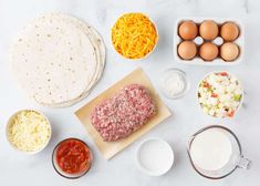 ingredients to make an appetizer laid out on a white counter top, including eggs, cheese and meat