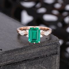 an emerald and diamond ring sitting on top of a wooden table