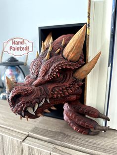 a close up of a fake dragon head on a wooden dresser with an open book in the background