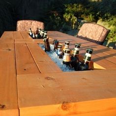 several bottles of beer sitting on top of a wooden table with chairs in the background