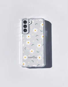 an iphone case with white daisies and green leaves on the back, sitting in front of a white background