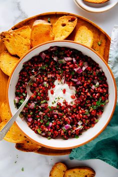 a bowl filled with pomegranate and topped with sour cream surrounded by tortilla chips