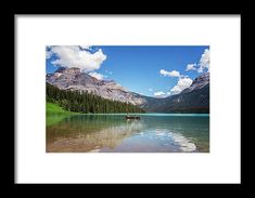 a lake surrounded by mountains and trees under a blue sky with clouds in the background