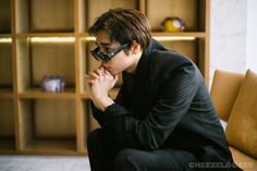 a man sitting on top of a brown couch wearing sunglasses and a suit jacket with his hands under his chin