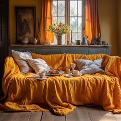 a couch covered in yellow linens with coffee cups and plates on it, next to a window