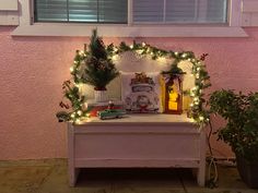 a white bench covered in christmas lights next to a potted plant and window sill