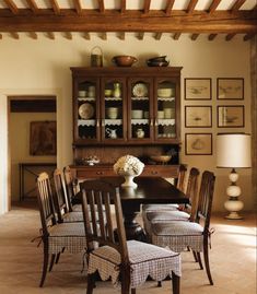 a dining room table with chairs and a vase on it's centerpiece in front of a wooden hutch