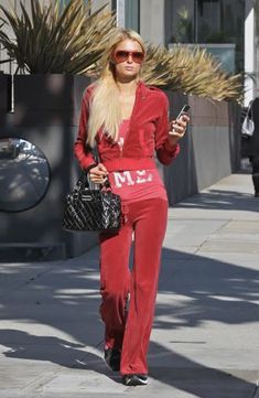 a woman in red is walking down the street while looking at her cell phone and holding a purse