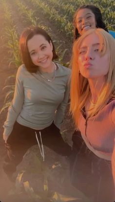 three young women standing next to each other in front of a cornfield at sunset