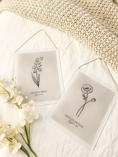 two glass coasters with flowers on them sitting on a white blanket next to a bouquet of flowers