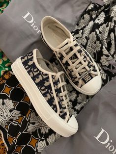 a pair of white shoes sitting on top of a black and white floral print bag