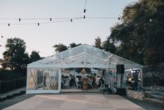 a group of people standing in front of a white tent with string lights hanging from the ceiling