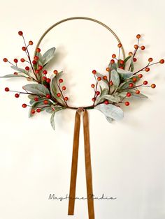 a wreath with red berries and green leaves hanging on a wall next to a brown ribbon