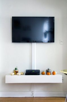 a flat screen tv mounted on the wall above a white shelf with candles and pumpkins