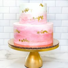 a pink and gold cake sitting on top of a metal stand next to a white tiled wall