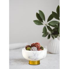 a marble bowl filled with fruit sitting next to a potted plant on a table