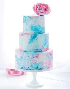 a three tiered cake with blue, pink and white marbled icing on it