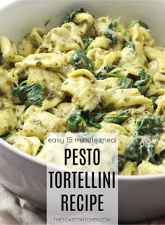 a white bowl filled with pasta and spinach on top of a table next to a napkin