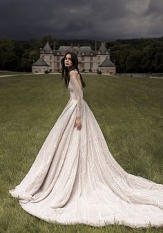 a woman in a wedding dress standing in the grass near a large building with dark clouds overhead