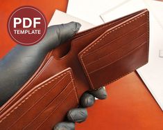 a hand holding a brown leather wallet on top of a red table next to a laptop