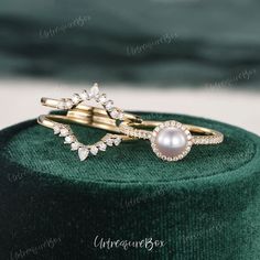 two rings on top of a green velvet box with diamonds and pearls in the middle