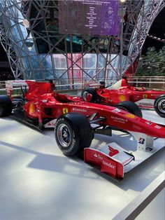 two red race cars on display in front of a large glass structure at the museum