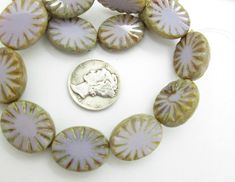 a coin is sitting next to some glass beads on a white surface with green and pink designs