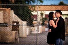 a man and woman standing next to each other in front of a chain link fence