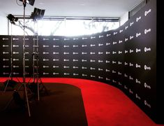 a camera set up in front of a red carpeted wall with words on it