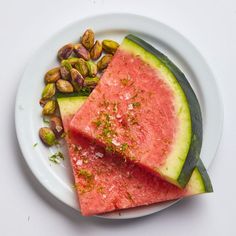 two slices of watermelon on a plate with pistachios and nuts