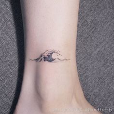 a small wave tattoo on the ankle is shown in black and grey colors, with an ocean wave coming out of it