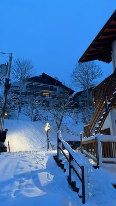 snow covered steps leading up to a ski lodge at night with the lights on in the distance