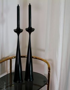 two black candles sitting on top of a glass table next to a white drapes