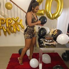 a woman standing in front of a table with black and gold balloons on top of it