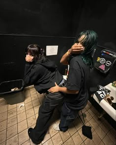 two people sitting in a bathroom with their backs to each other and one person covering his face