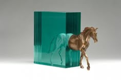 a toy horse is standing in front of a green glass block on a white surface