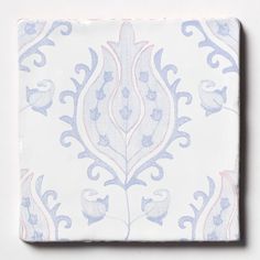 a white and blue square tile with an ornate design on the bottom, in front of a white background