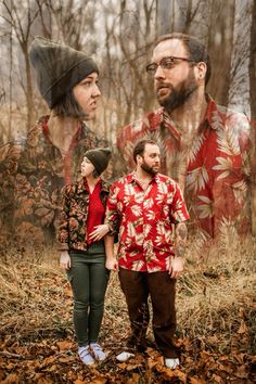 two men and a woman standing in the woods with trees behind them, one man is wearing