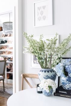 a white table topped with blue and white vases filled with flowers next to a chair